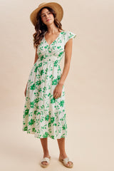 woman wearing a white floral midi dress with green accents and cap sleeves, paired with a straw hat and espadrilles