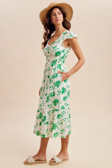 woman wearing a white floral midi dress with green leaves and ruffles, paired with a straw hat and espadrille sandals