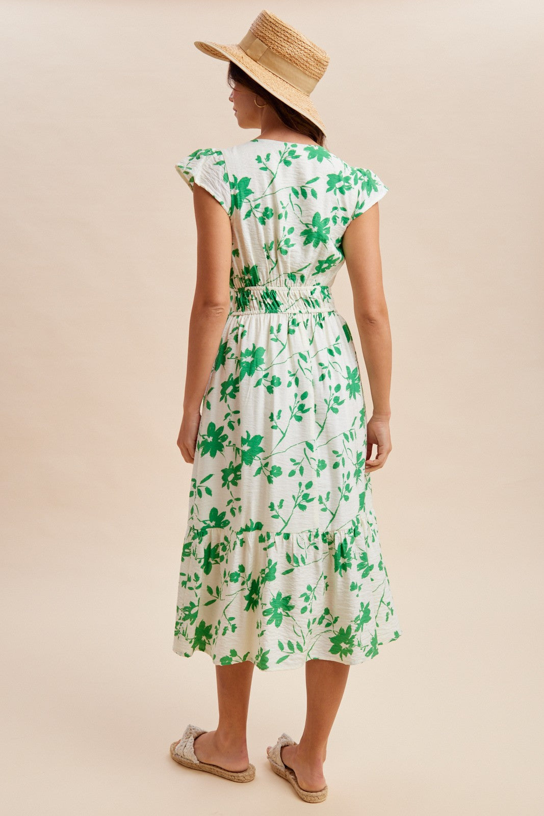 woman wearing a green floral midi dress with ruffled sleeves and smocked waist, standing with her back to the camera