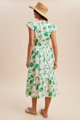 woman wearing a green floral midi dress with ruffled sleeves and smocked waist, standing with her back to the camera