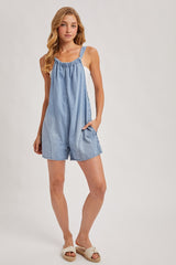 woman wearing a light blue denim romper with adjustable straps and pockets, styled with brown sandals