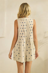 woman wearing a beige sleeveless romper with navy polka dots and pleating at the back