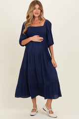 woman wearing a navy blue maternity dress with puff sleeves and a babydoll silhouette, holding her baby bump
