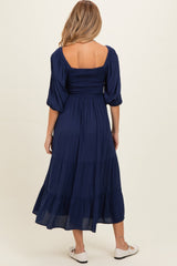 woman wearing a navy blue maternity dress with a smocked bodice and tiered skirt, viewed from the back