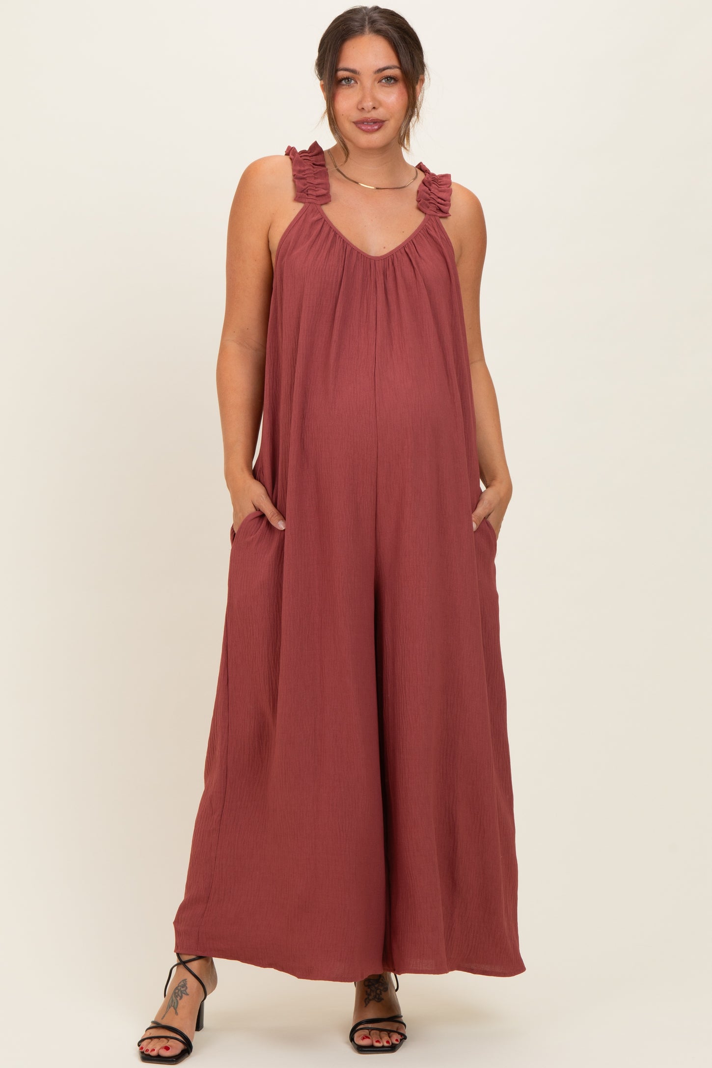 woman wearing a rust ruffled strap maternity jumpsuit with pockets and a visible baby bump