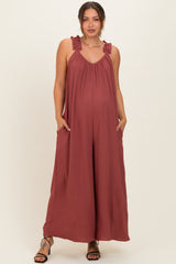 woman wearing a rust ruffled strap maternity jumpsuit with pockets and a visible baby bump