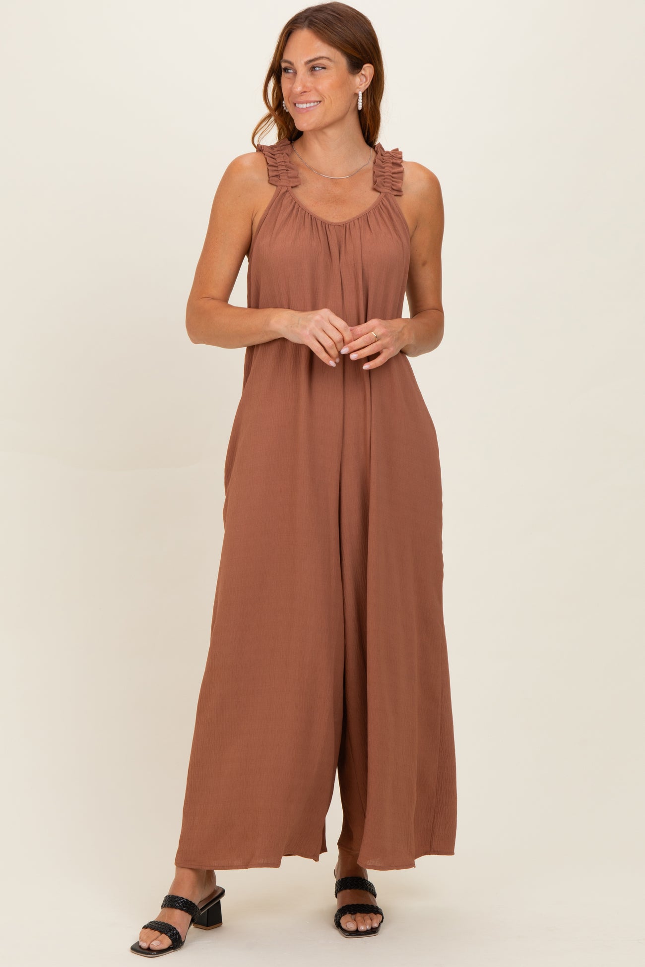 woman wearing a rust-colored sleeveless jumpsuit with ruffle details on the straps and a flowy silhouette