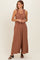 woman wearing a rust-colored sleeveless jumpsuit with ruffle details on the straps and a flowy silhouette