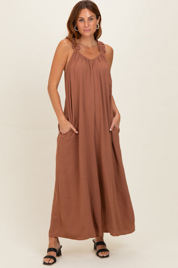 woman wearing a rust-colored maxi dress with adjustable straps and pockets, styled with black sandals