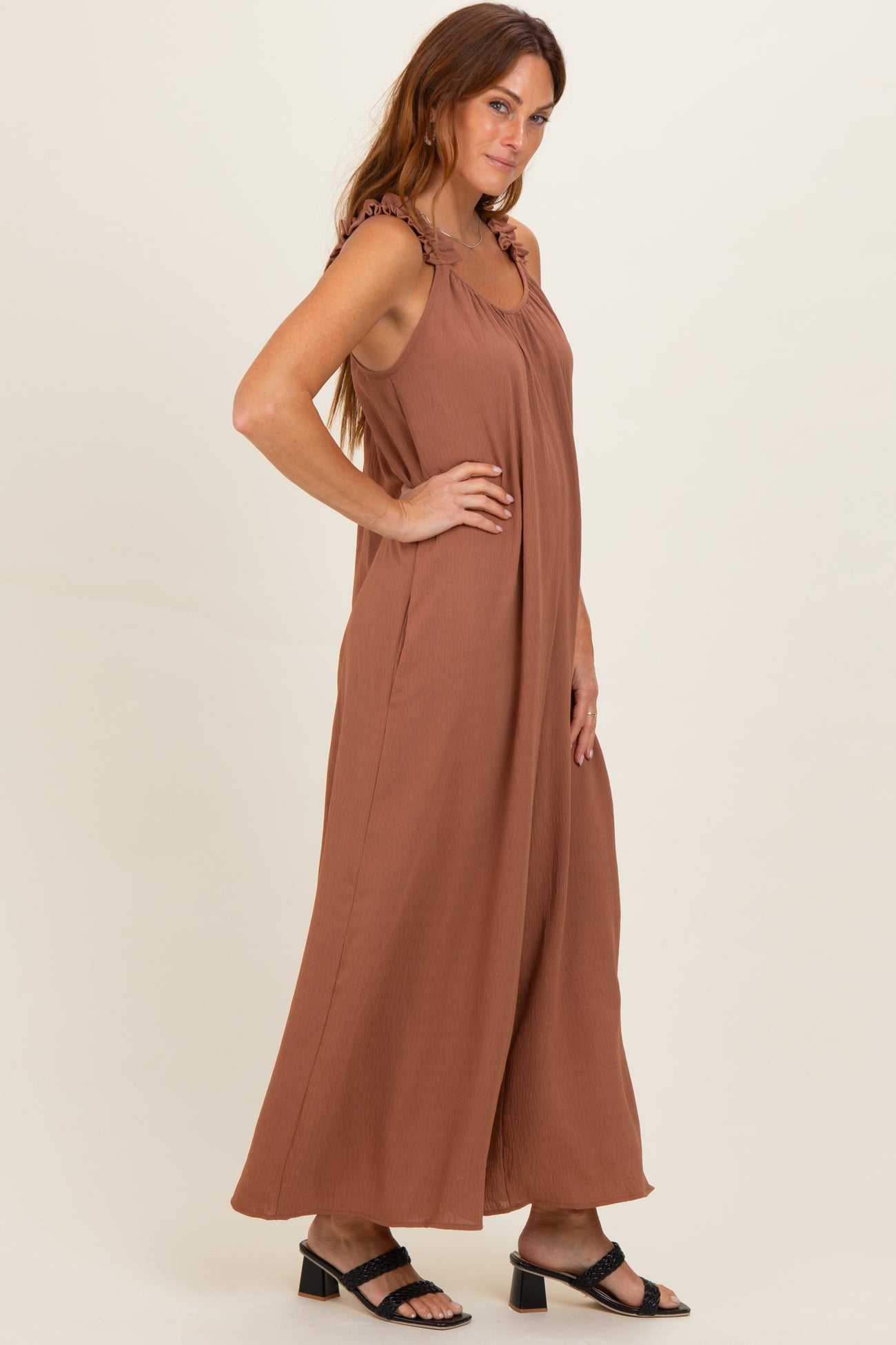 woman wearing a brown sleeveless jumpsuit with ruffle straps and side pockets