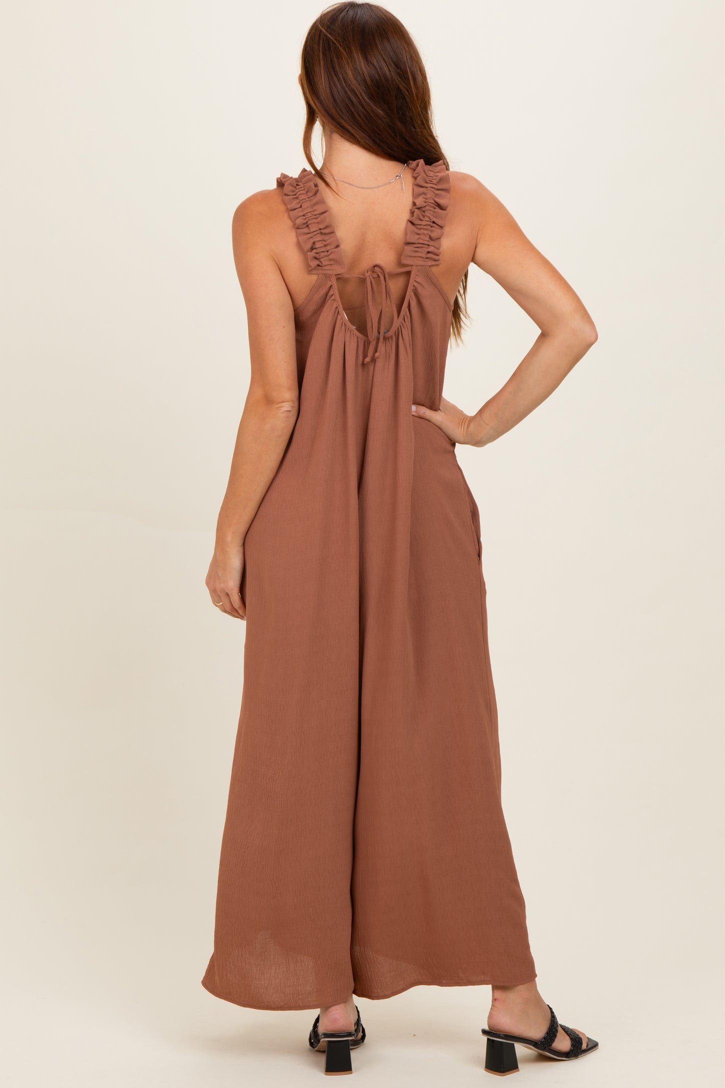 woman wearing a rust brown sleeveless maxi dress with ruffled straps and a tie back detail