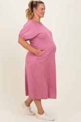 woman wearing a pink maternity plus midi dress with short sleeves and pockets, showing her baby bump