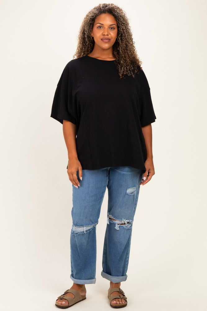 woman wearing a black oversized t-shirt and distressed blue jeans, standing against a neutral background
