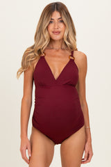 woman wearing a burgundy maternity swimsuit with a plunging neckline and adjustable straps, showcasing her baby bump