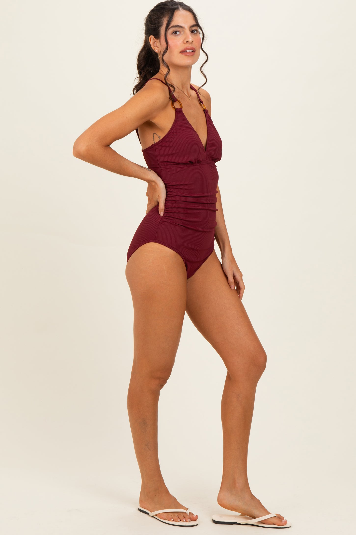 woman wearing a burgundy one-piece swimsuit with adjustable straps and a plunging neckline
