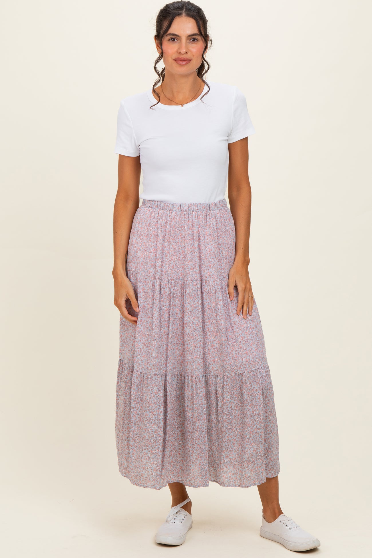 woman wearing a white short sleeve top and a pink floral tiered maxi skirt with white sneakers
