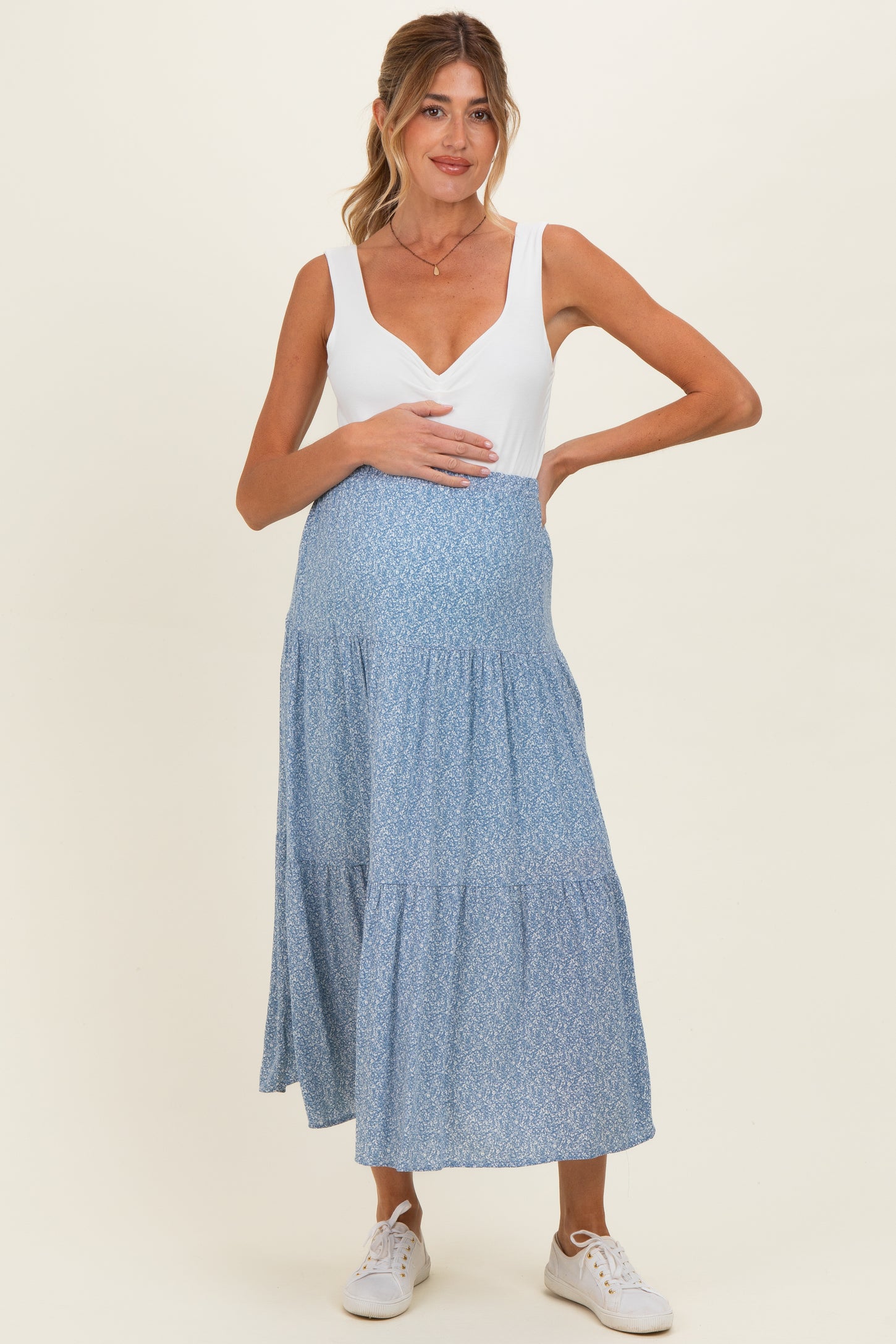 woman wearing a white v-neck maternity dress with a blue floral skirt and holding her baby bump