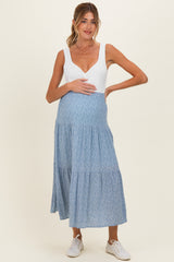 woman wearing a white v-neck maternity dress with a blue floral skirt and holding her baby bump