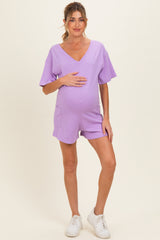woman wearing a lavender maternity romper with short sleeves and pockets, holding her baby bump