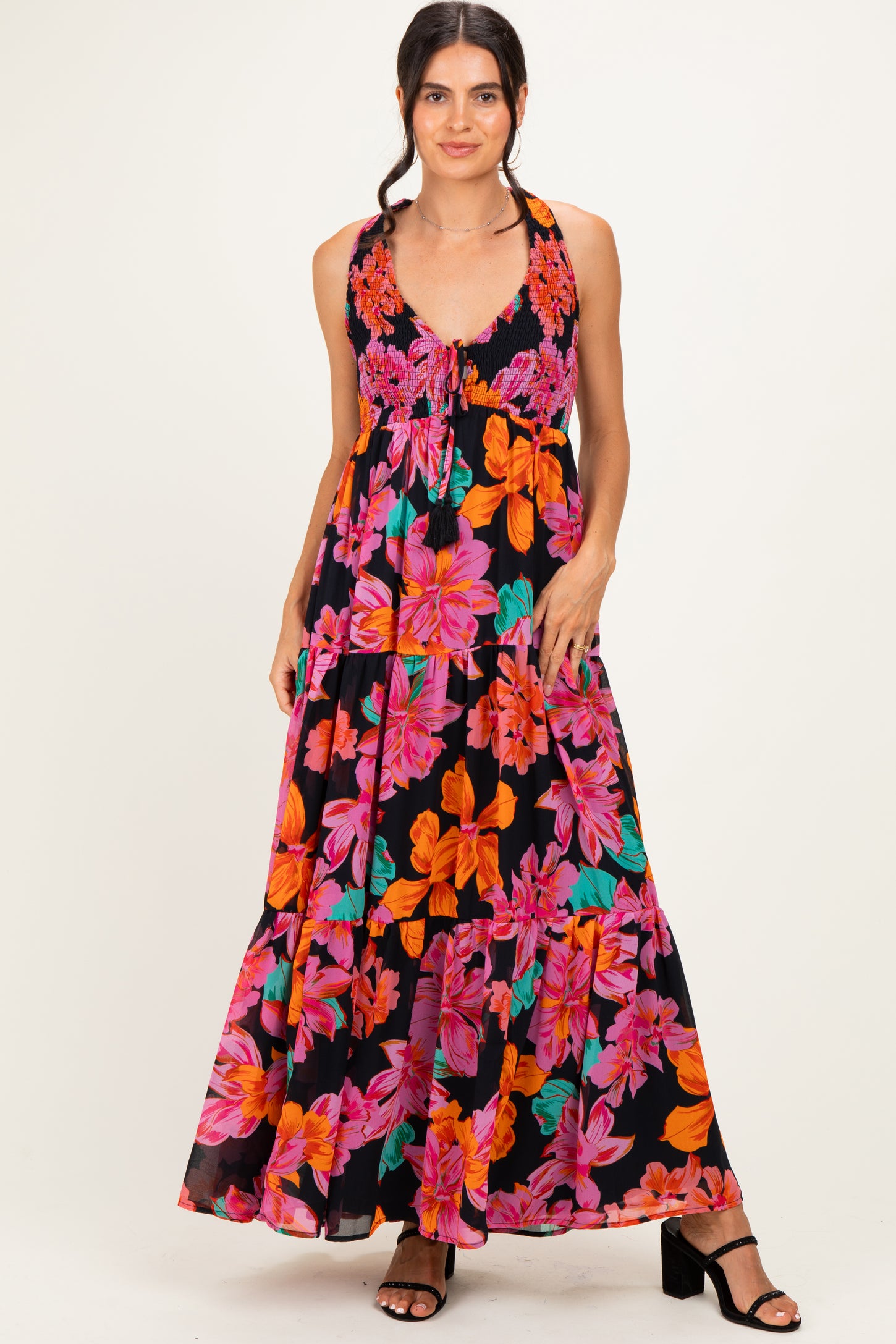 woman wearing a black floral maxi dress with vibrant pink and orange flowers and a tiered skirt, posing with one hand on her hip