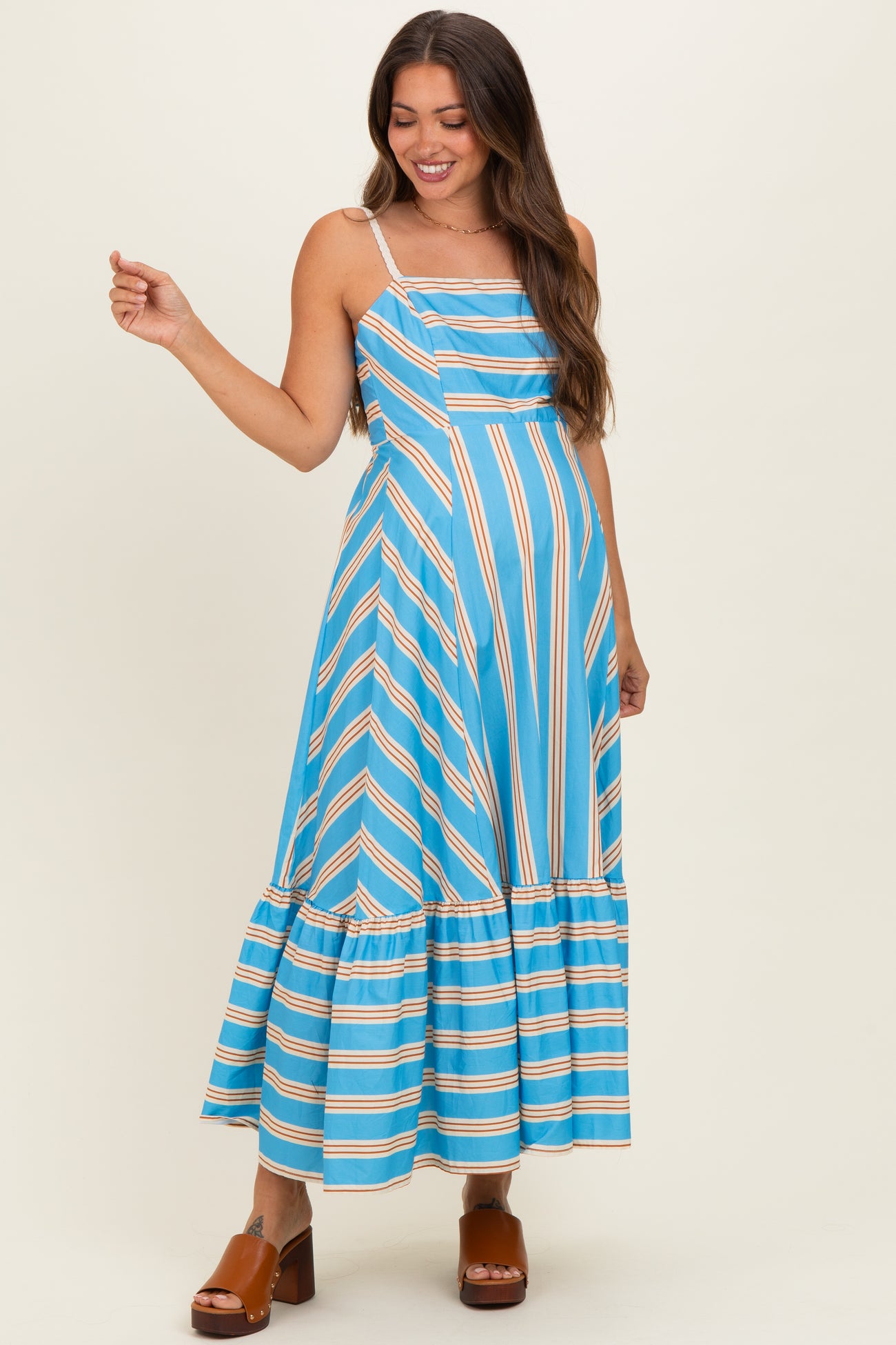woman wearing a blue and orange striped maternity dress with a flared hem and spaghetti straps, showcasing her baby bump