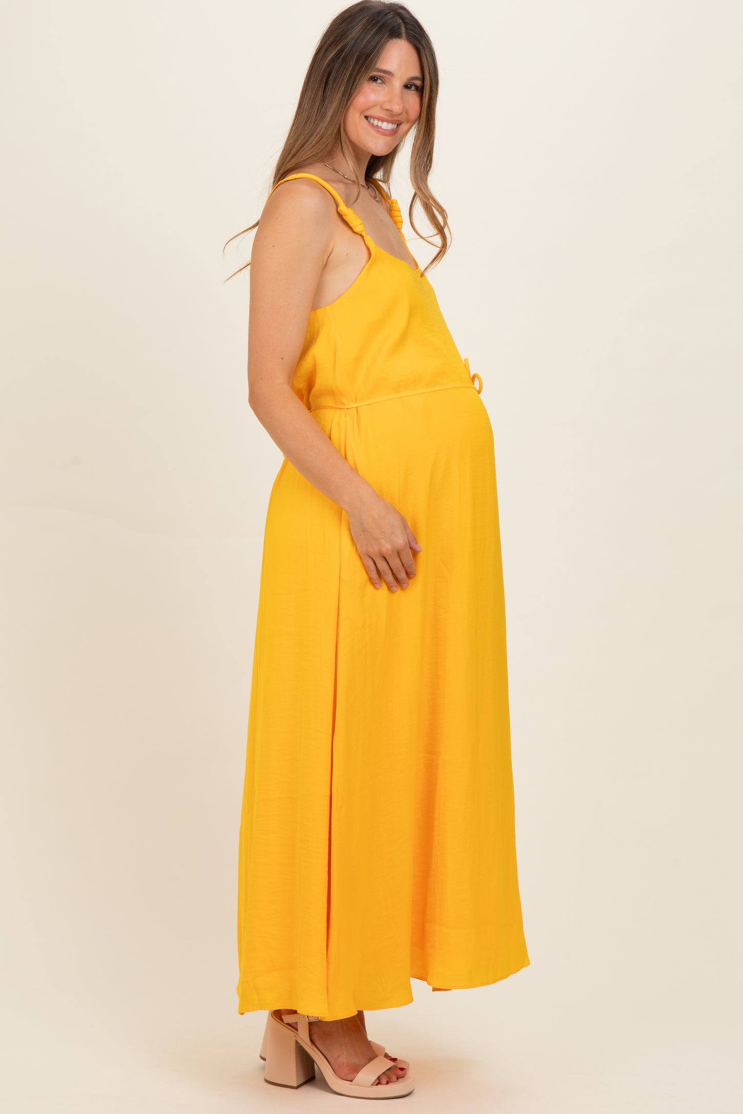 woman wearing a yellow sleeveless maternity maxi dress with a drawstring waist and visible baby bump