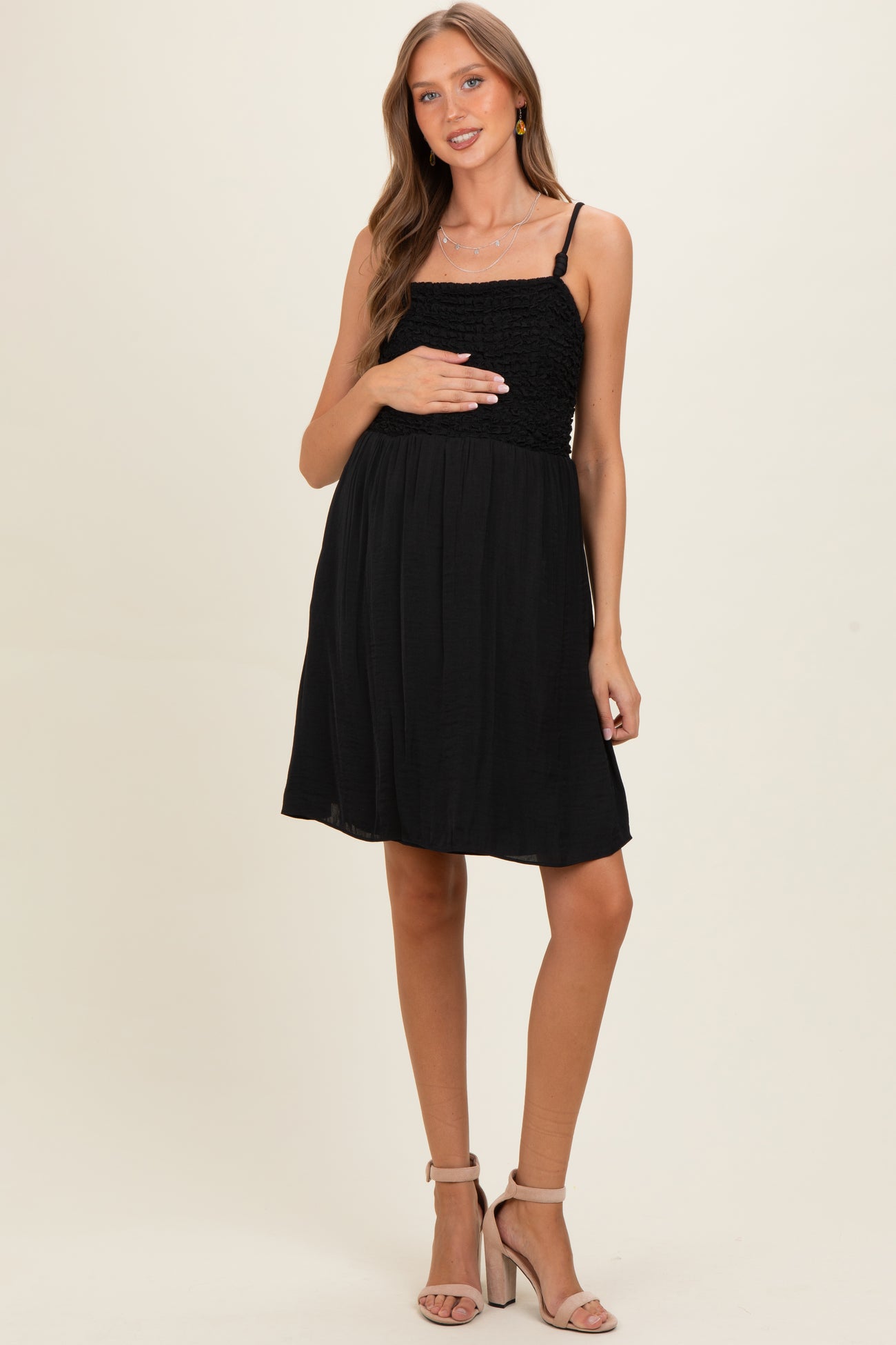 woman wearing a black maternity dress with smocked bust and spaghetti straps, holding her baby bump