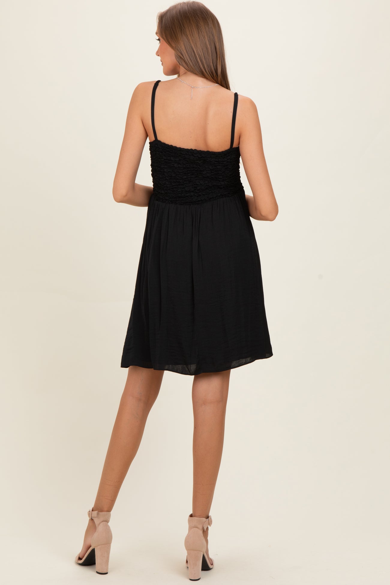 woman wearing a black maternity dress with a smocked bodice and flowing skirt, seen from the back