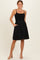 woman wearing a black smocked sundress with adjustable straps and pockets, standing against a neutral background