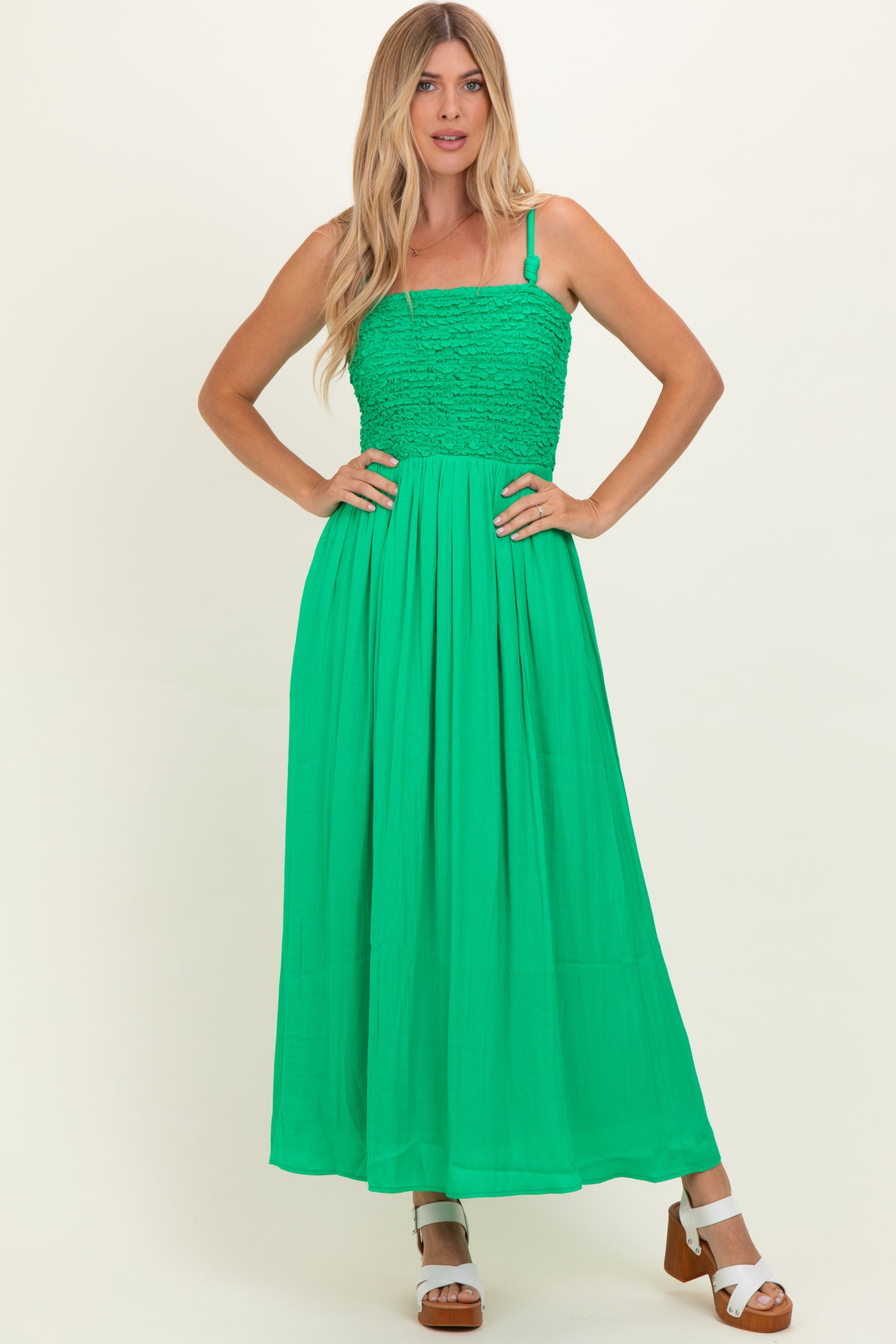 woman wearing a green maxi dress with a smocked bodice and adjustable straps, standing with her hands on her hips