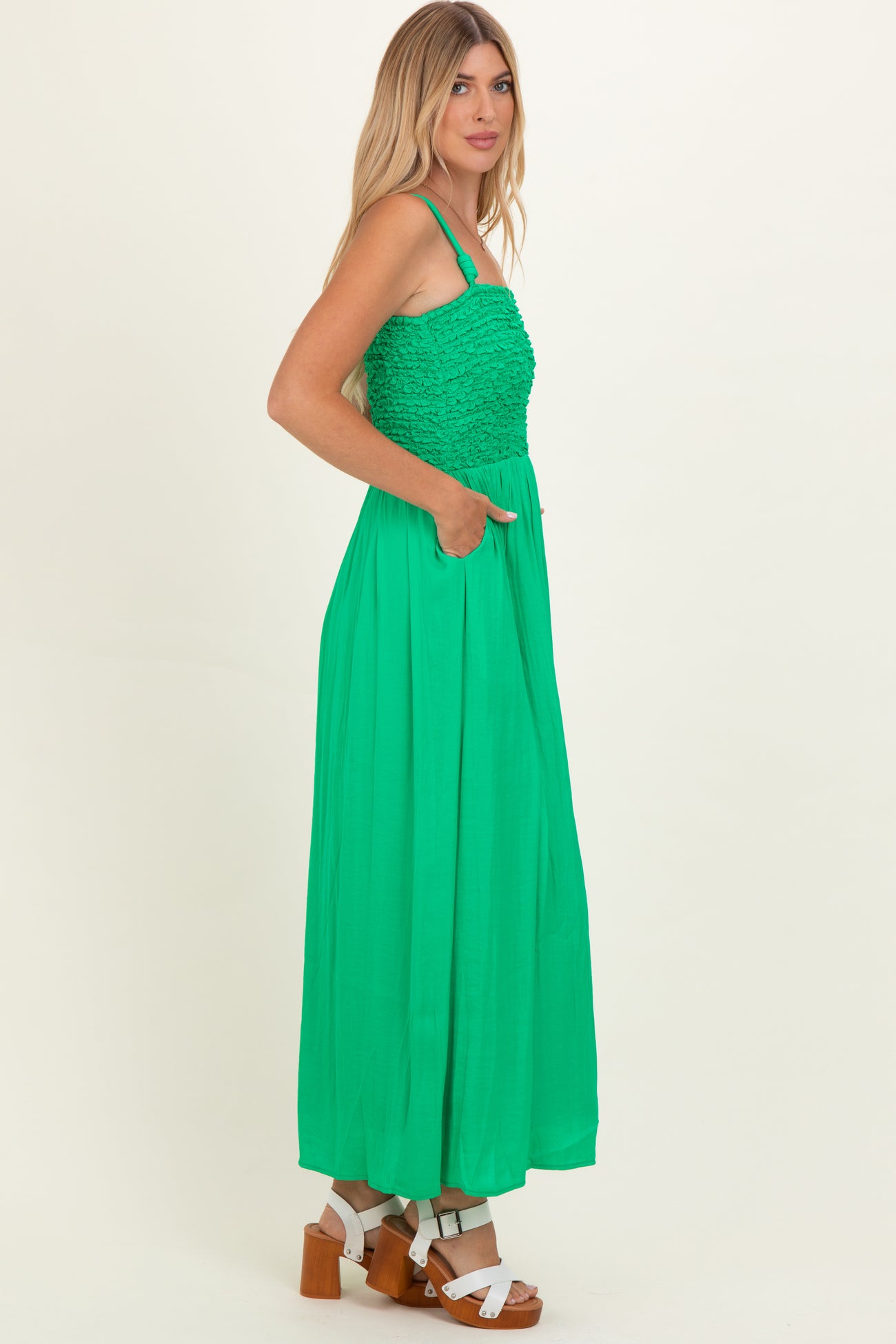 woman wearing a bright green maxi dress with a textured bodice and side pockets, paired with chunky heels