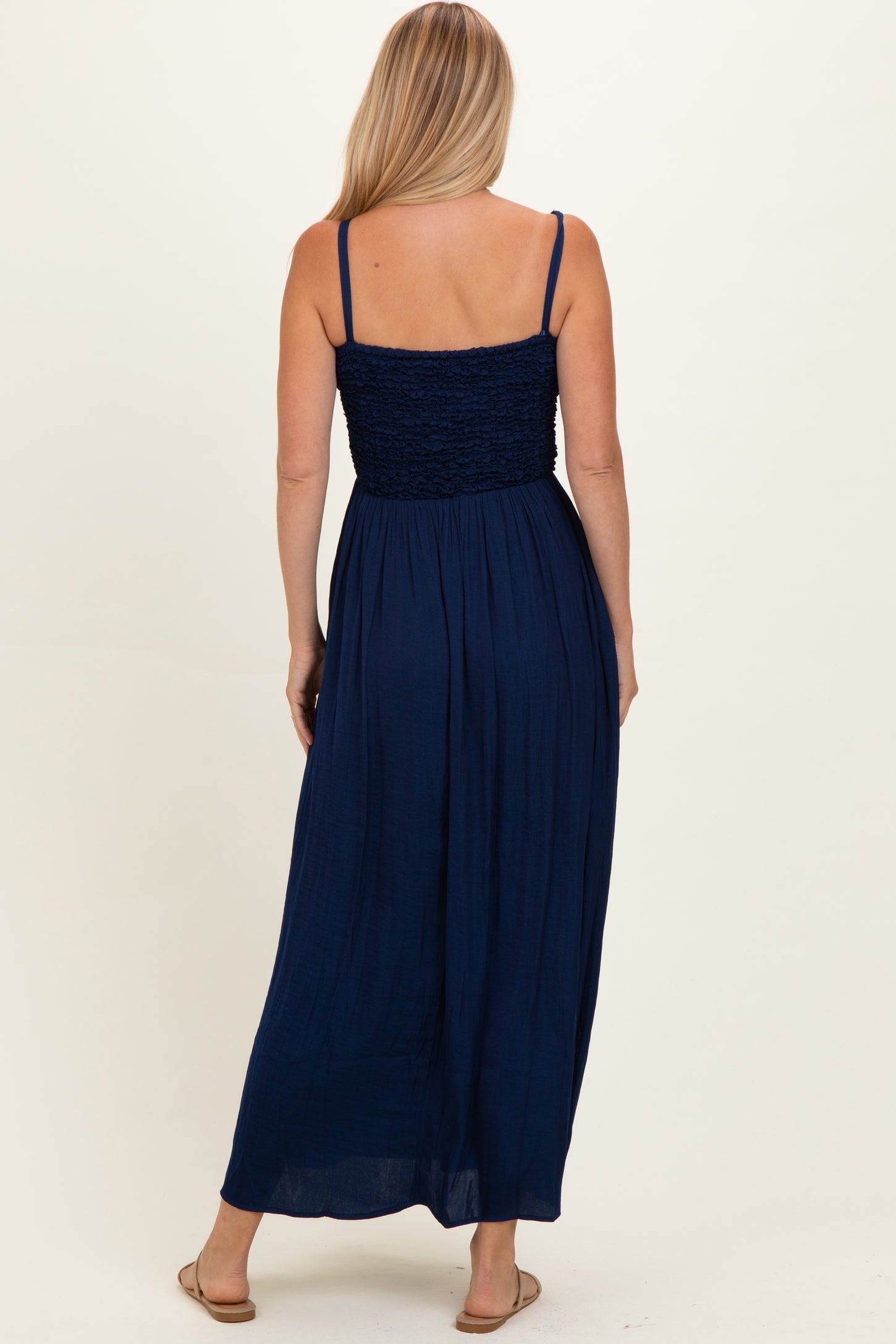 woman wearing a navy blue maxi dress with a smocked bodice and spaghetti straps, seen from the back