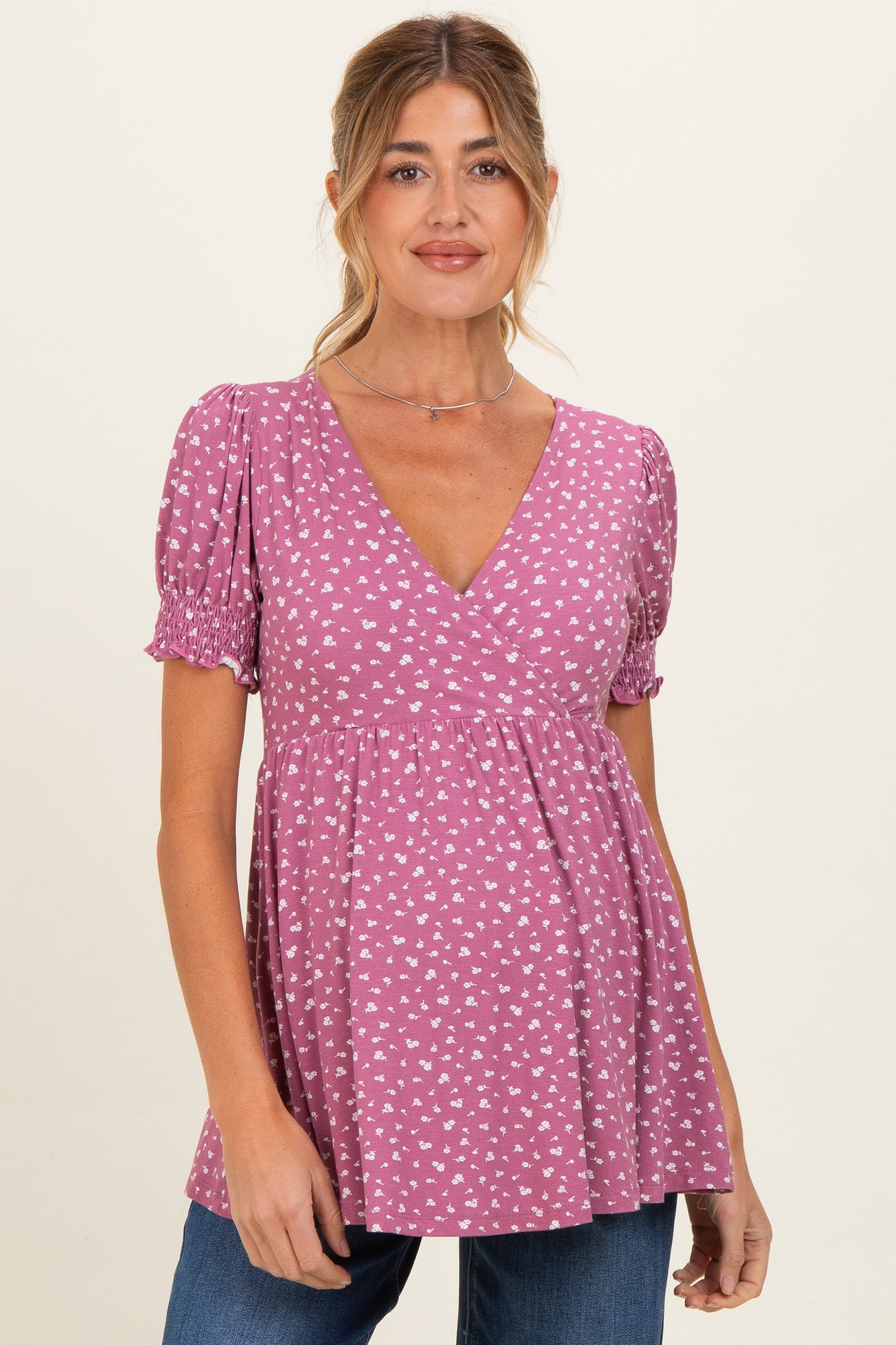 woman wearing a pink short sleeve maternity top with a v-neck and heart print, smiling at the camera