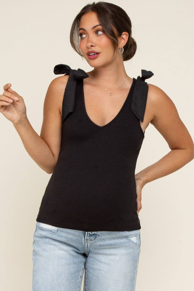 woman wearing a black sleeveless maternity top with bow tie straps and a deep v-neck, paired with light blue jeans
