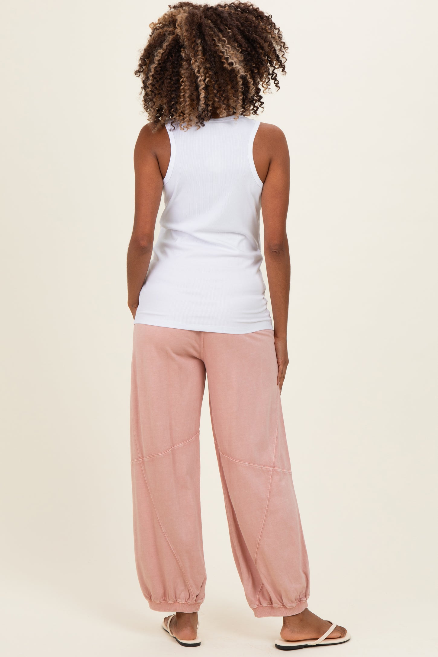 woman wearing a white sleeveless maternity top and loose pink maternity pants, showing a relaxed back view