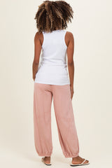 woman wearing a white sleeveless maternity top and loose pink maternity pants, showing a relaxed back view