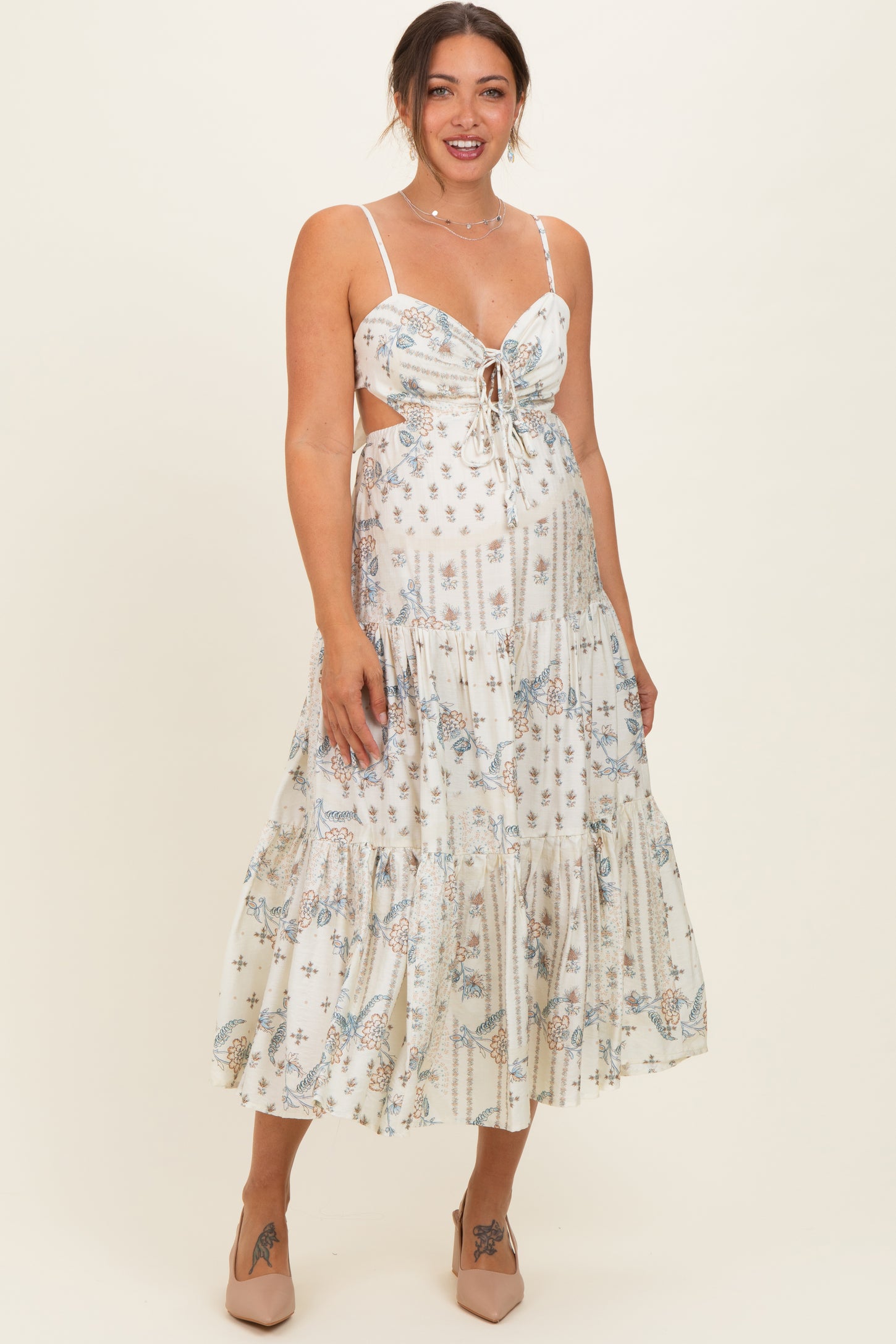 woman wearing a white floral print maternity maxi dress with a tied front and spaghetti straps, smiling at the camera