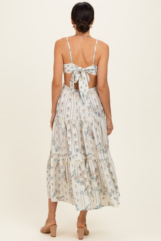 woman wearing a floral printed maxi dress with a tie back and tiered skirt, showing off the back design