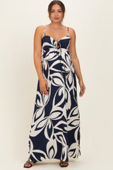 woman wearing a navy blue and white floral print maternity maxi dress with a tie front detail and spaghetti straps, showcasing her baby bump