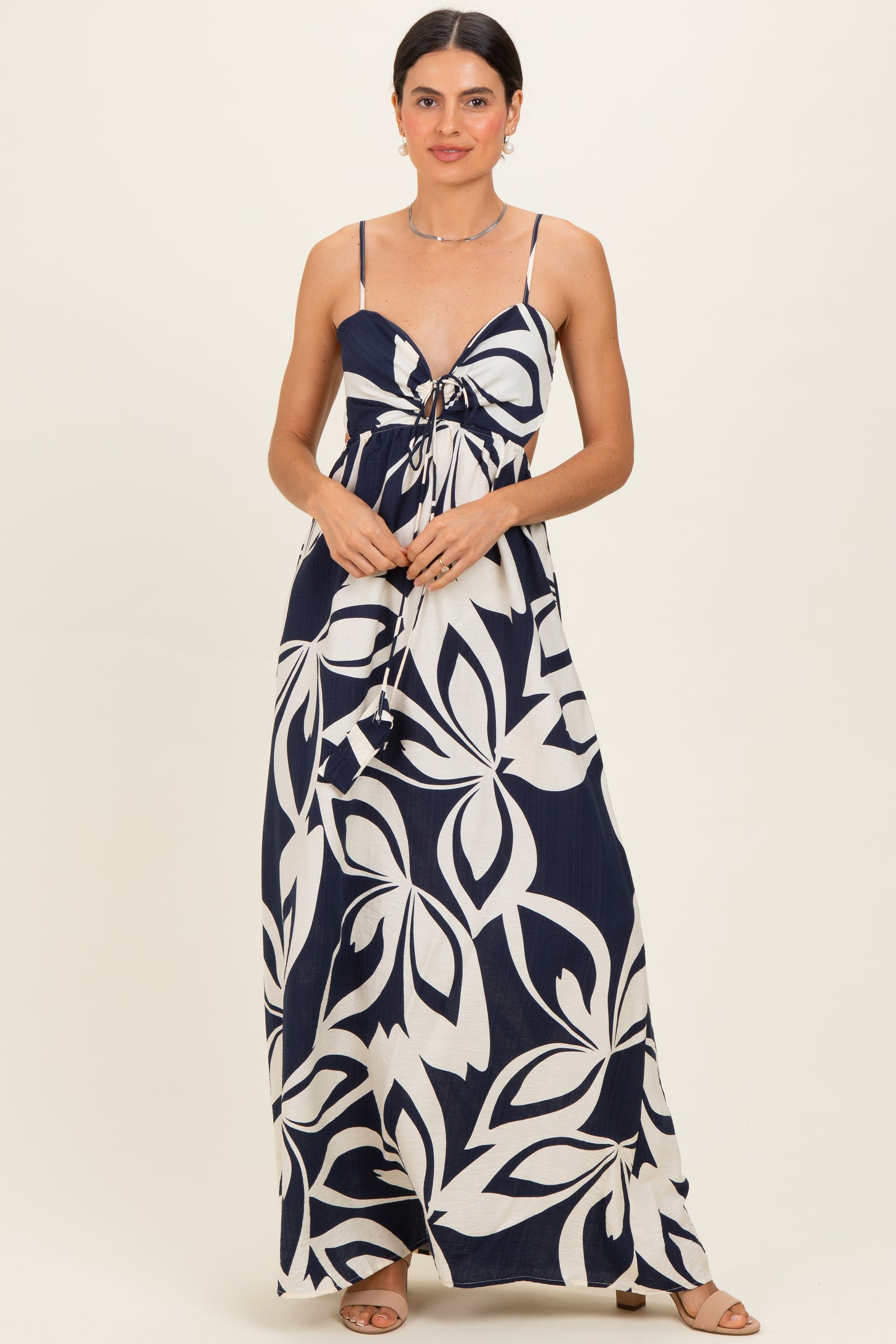 woman wearing a navy blue and white floral print maxi dress with a front tie detail and spaghetti straps