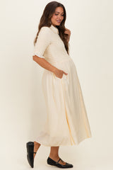 woman wearing a cream-colored maternity dress with a smocked bodice and side pockets, showcasing her baby bump