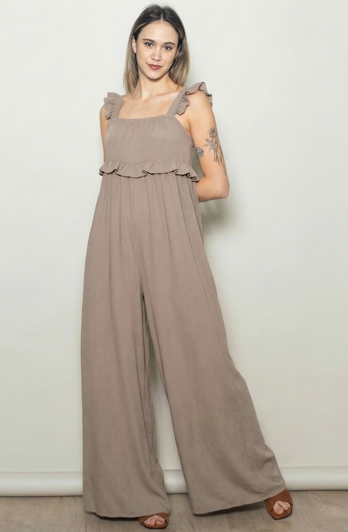 woman wearing a taupe ruffled strap jumpsuit with a flowy silhouette and wide leg style