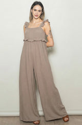 woman wearing a taupe ruffled strap jumpsuit with a flowy silhouette and wide leg style