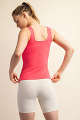 woman wearing a pink tank top and white bike shorts, seen from the back, adjusting the shorts