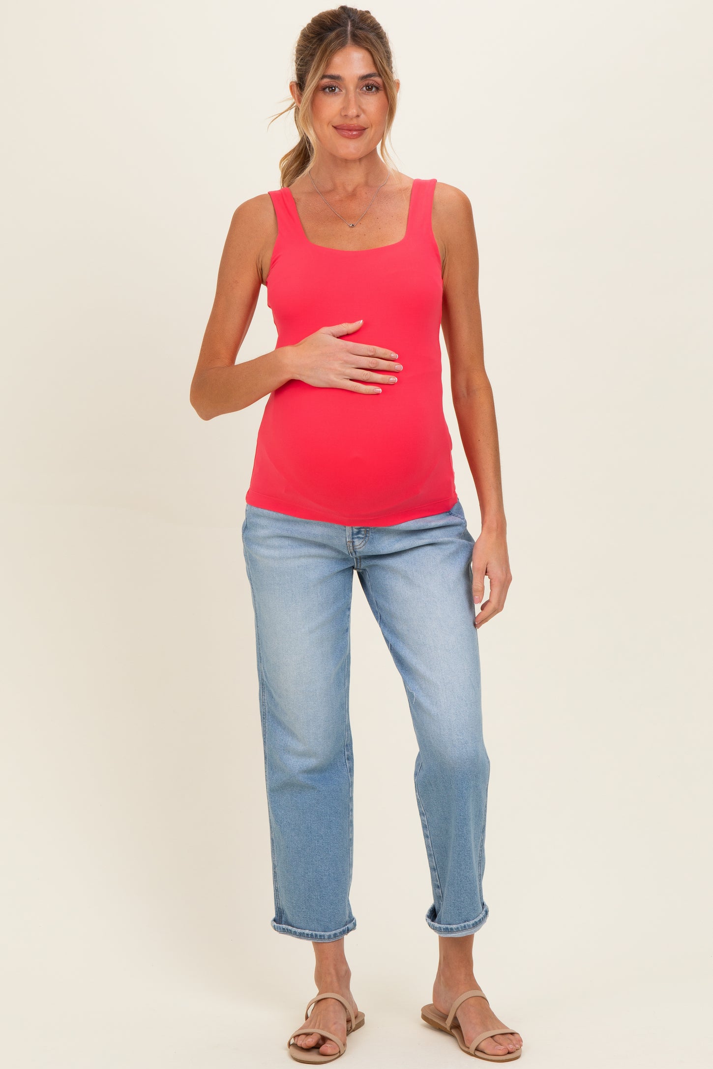 woman wearing a bright pink maternity tank top and light blue jeans, holding her baby bump