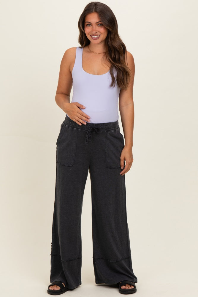 woman wearing a light purple maternity tank top and gray wide-leg maternity lounge pants, holding her baby bump