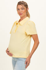 woman wearing a yellow short sleeve maternity top with puffed sleeves and collar, showing her baby bump