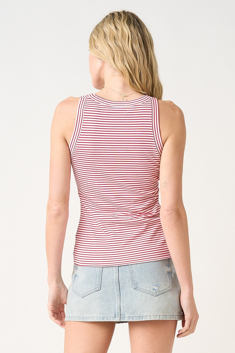 woman wearing a red and white striped tank top with a fitted style and back view, paired with a denim mini skirt