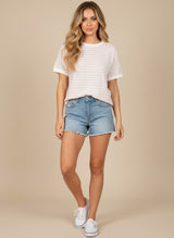 woman wearing a striped short sleeve top with a round neckline and denim shorts, standing in white sneakers