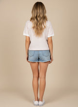 woman wearing a white short sleeve top with pink stripes and blue denim shorts, viewed from the back
